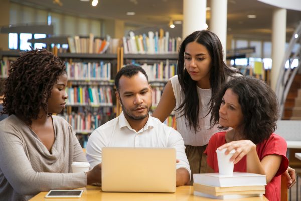 Concentrated young people reading information from laptop. Cheerful students working with laptop at library. Education concept